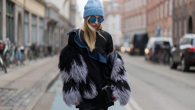Mulher loira com óculos escuros veste um casaco de pele preto com cinza.