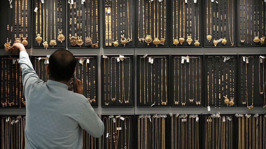 一名男子手持電話,背後展示著大量的金器。