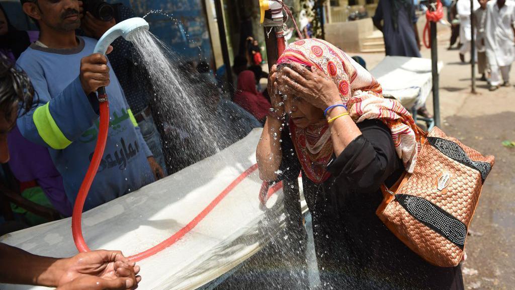 Una mujer con un pañuelo en la cabeza siendo rociada con agua.