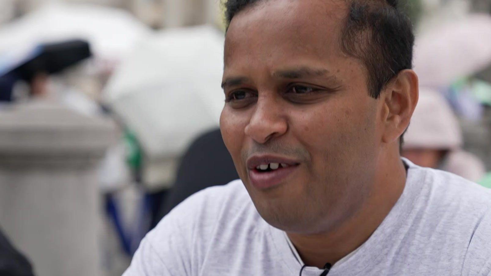 Pai de Bodhana dando entrevista. Ele usa uma camisa branca 