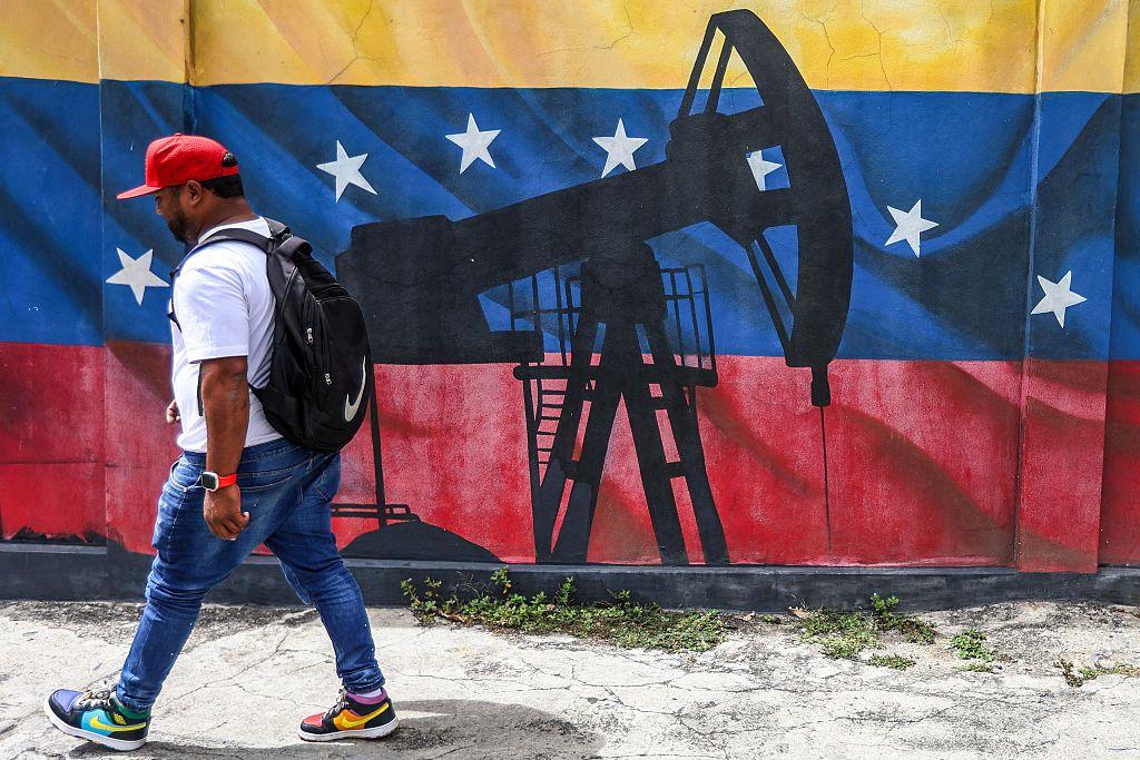 Un hombre pasa por un mural de un balancín de petróleo que tiene como fondo la bandera de Venezuela.
