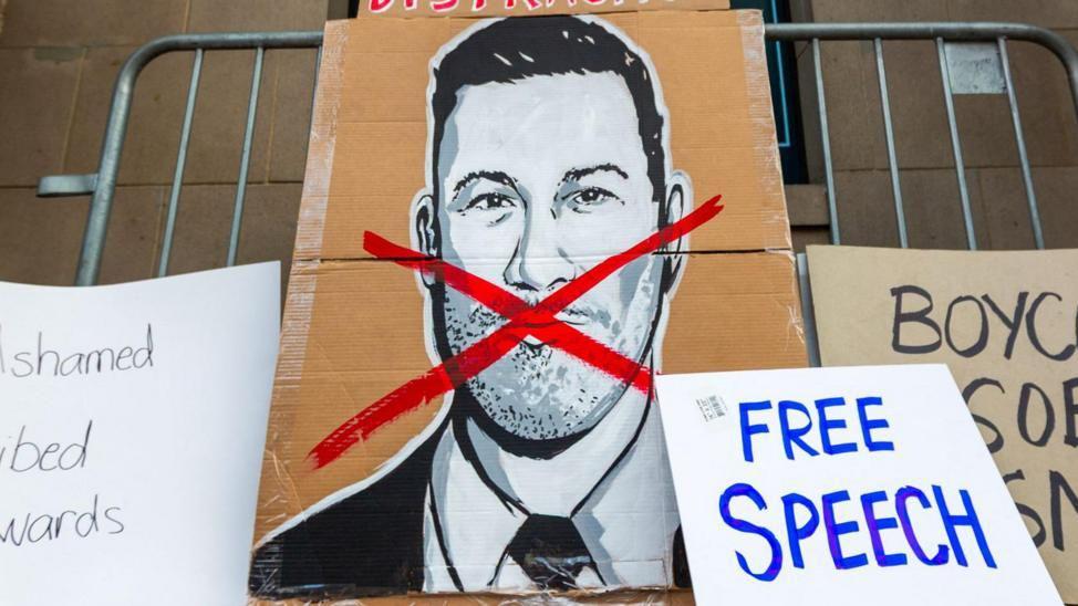 Un gran cartel de cartón con una ilustración de Jimmy Kimmel y una cruz roja en su rostro, junto a otros carteles, incluido uno que dice "libertad de expresión".