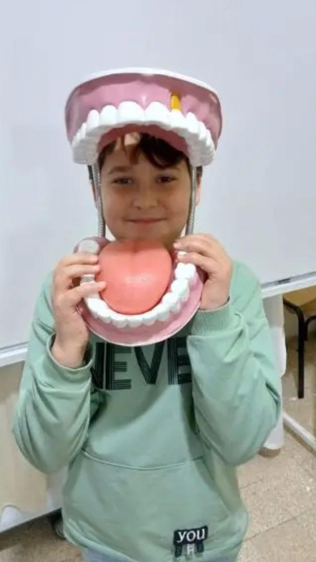 Qassem, de ojos marrones, el pelo peinado y una sudadera verde, sonríe a la cámara a través de una réplica gigante de dientes, encías y lengua, en su colegio, en el Líbano.