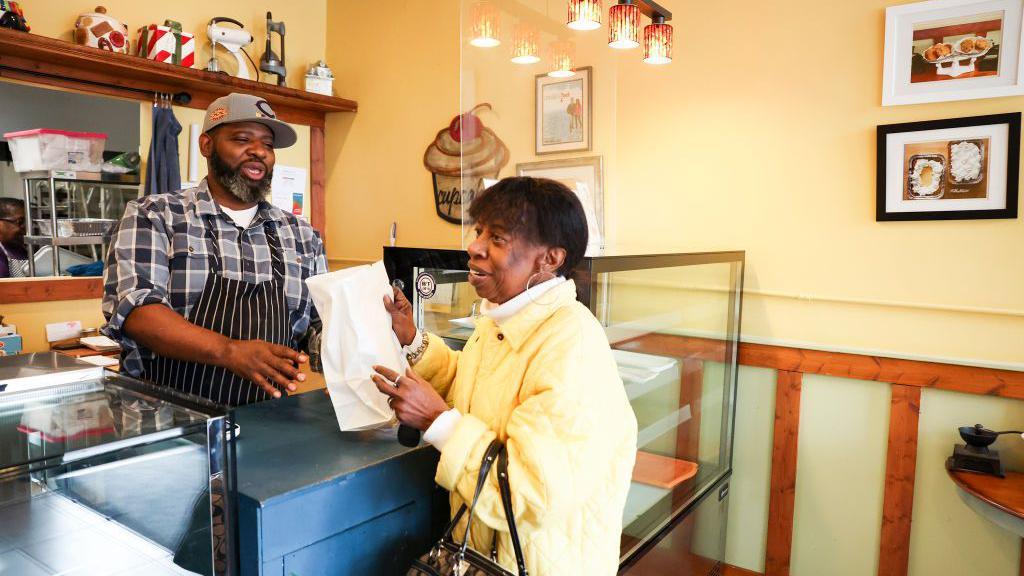Hunter no caixa da padaria, conversando com uma cliente que acaba de atender