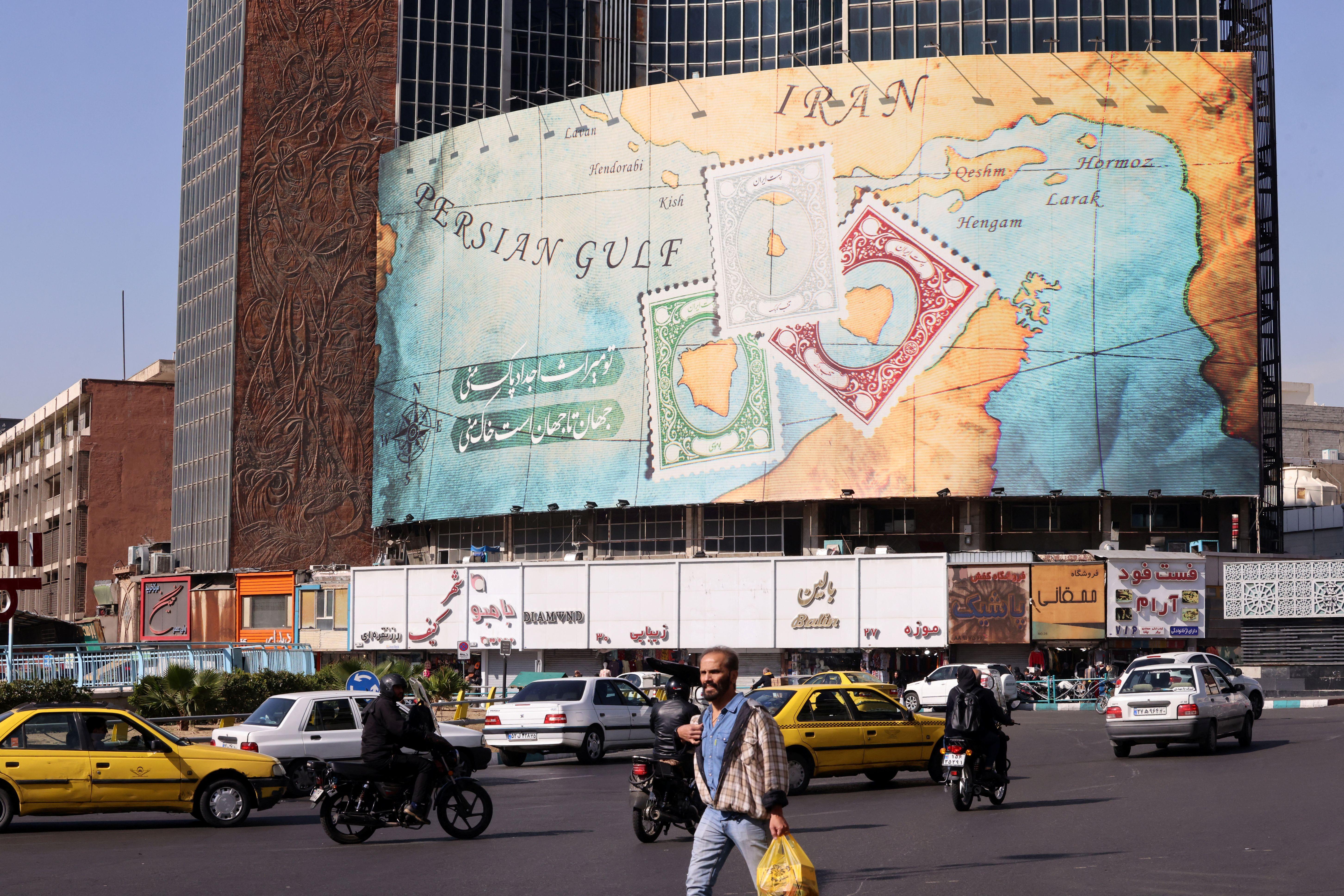 أشخاص ومركبات يمرّون أمام لوحة إعلانية تغطي واجهة مبنى في ساحة ولي عصر في طهران، تُصوَّر عليها جزر أبو موسى وطنب الكبرى وطنب الصغرى المتنازع عليها على هيئة طوابع بريدية. وتخضع الجزر الثلاث لسيطرة إيران منذ عام 1971، بينما تطالب الإمارات بالسيادة عليها.