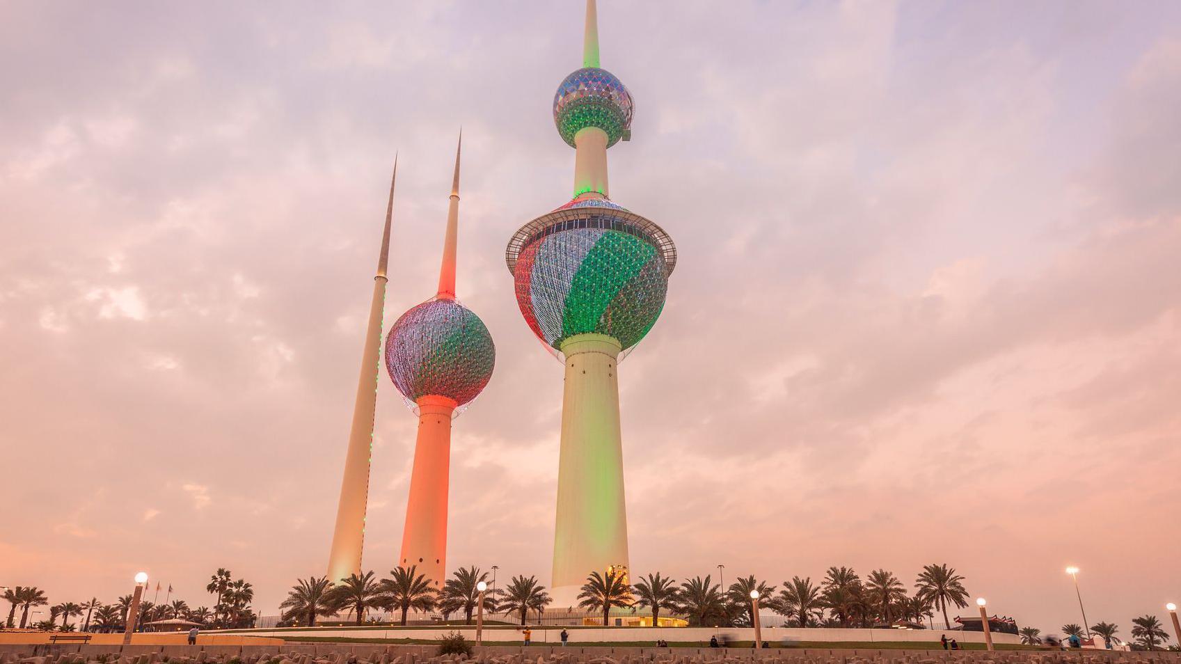 صورة لأبراج الكويت عند المغيب وهي مضاءة بعلم الكويت.