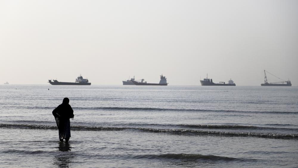Una mujer en una playa de Irán frente a varios buques en el estrecho de Ormuz