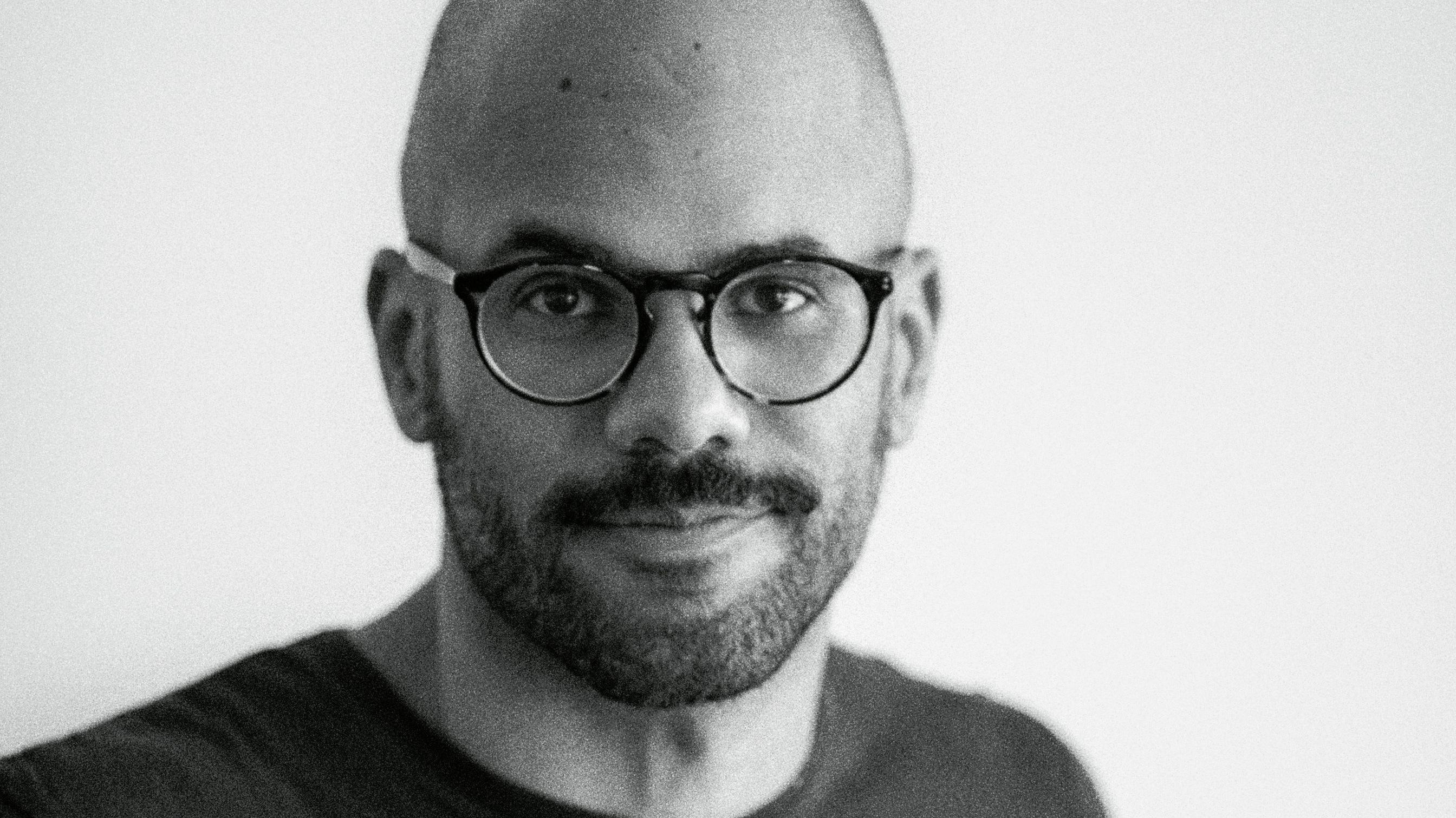 Kau&ecirc; Lopes dos Santos, um homem careca, de barba curta e &oacute;culos, vestindo camiseta escura, em foto de rosto tirada com &acirc;ngulo fechado