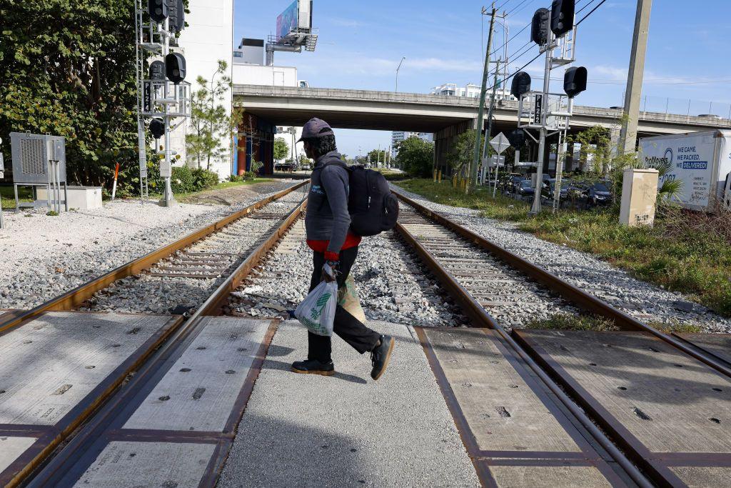Una persona con gorra y mochila a la espalda cruza las vás del Brightline en Miami. 