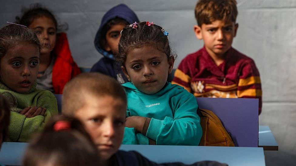 Niños pequeños sentados en una escuela temporal en una tienda de campaña.