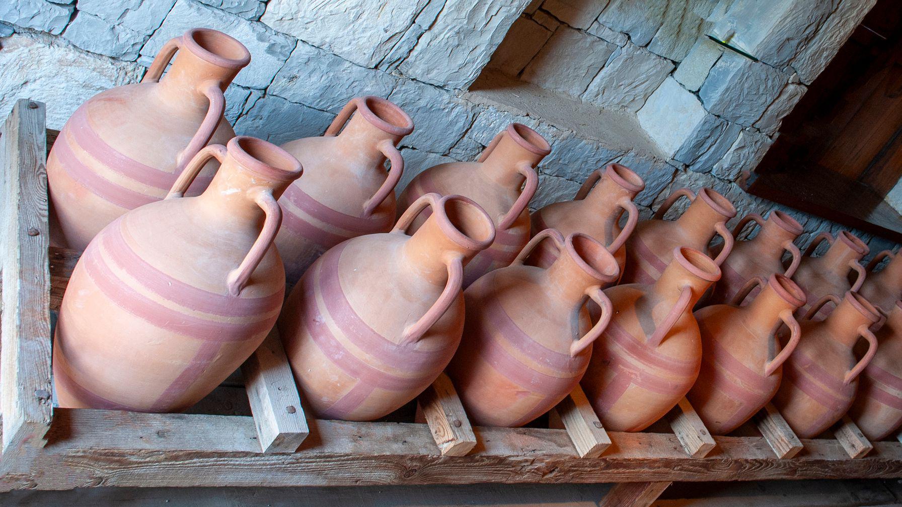 Diversas ânforas de argila em uma armação de madeira no chão