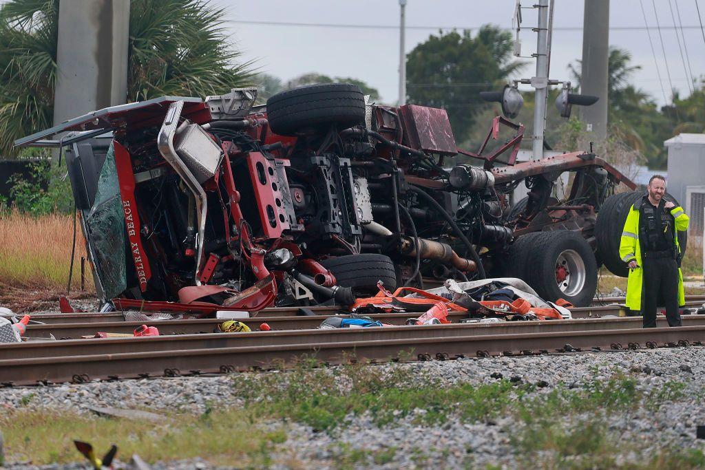Un camión de bomberos volcado y destrozado junto a las vías de un tren. Junto a él, un agente. 