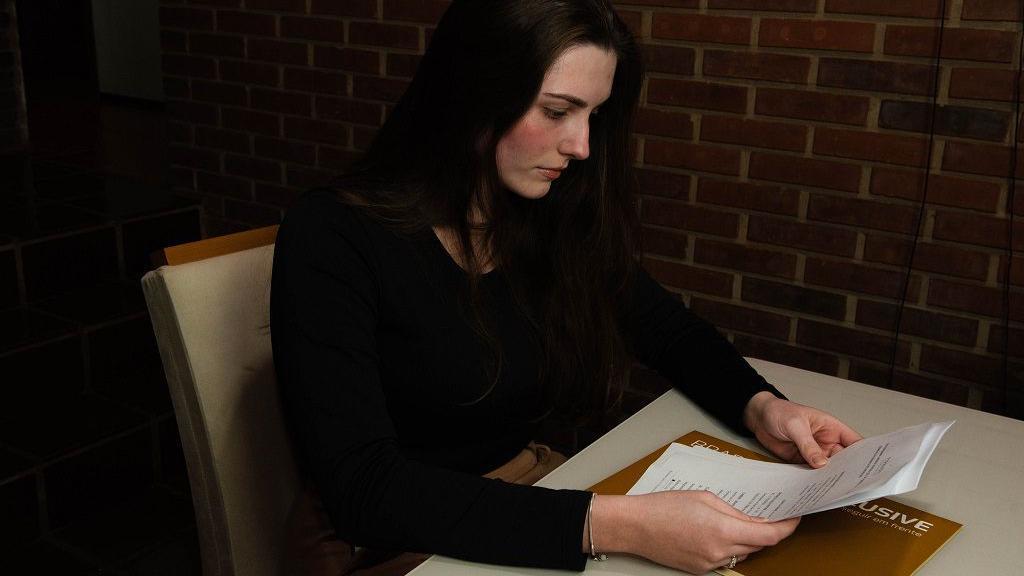 Michele olhando para papéis em cima da mesa