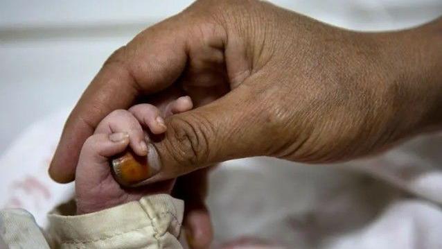 يد مولود تتشبث بإصبع كبير يداعبه.