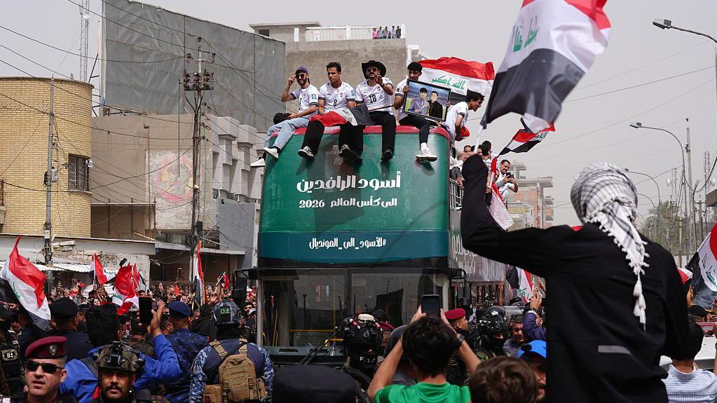 حافلة خضراء تقل لاعبي منتخب العراق، تحيط بها الجماهير وأعلام البلاد في شوارع بغداد، خلال الاحتفالات بالتأهل إلى كأس العالم 2026.