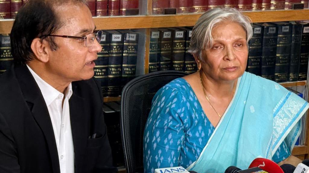 Retired judge Giribala Singh seen in a blue sari - a lawyer is seated next to her in his black and white uniform