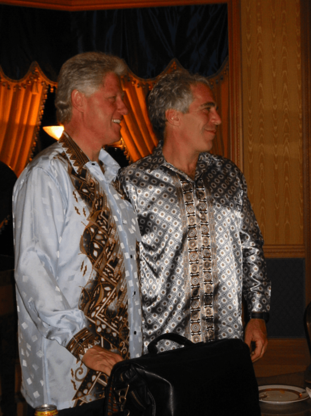 Bill Clinton e Jeffrey Epstein posam lado a lado, olhando para a direita da c&acirc;mera, ambos vestindo camisas de seda com estampa paisley.