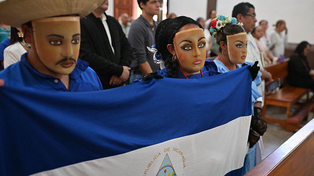 Nicaragüenses en el exilio con el rostro cubierto, sosteniendo una bandera nicaragüense, asisten a misa en la Iglesia de San Francisco en San José, Costa Rica, el 19 de abril de 2026. El servicio conmemora el aniversario del levantamiento social y político de 2018 en Nicaragua.
