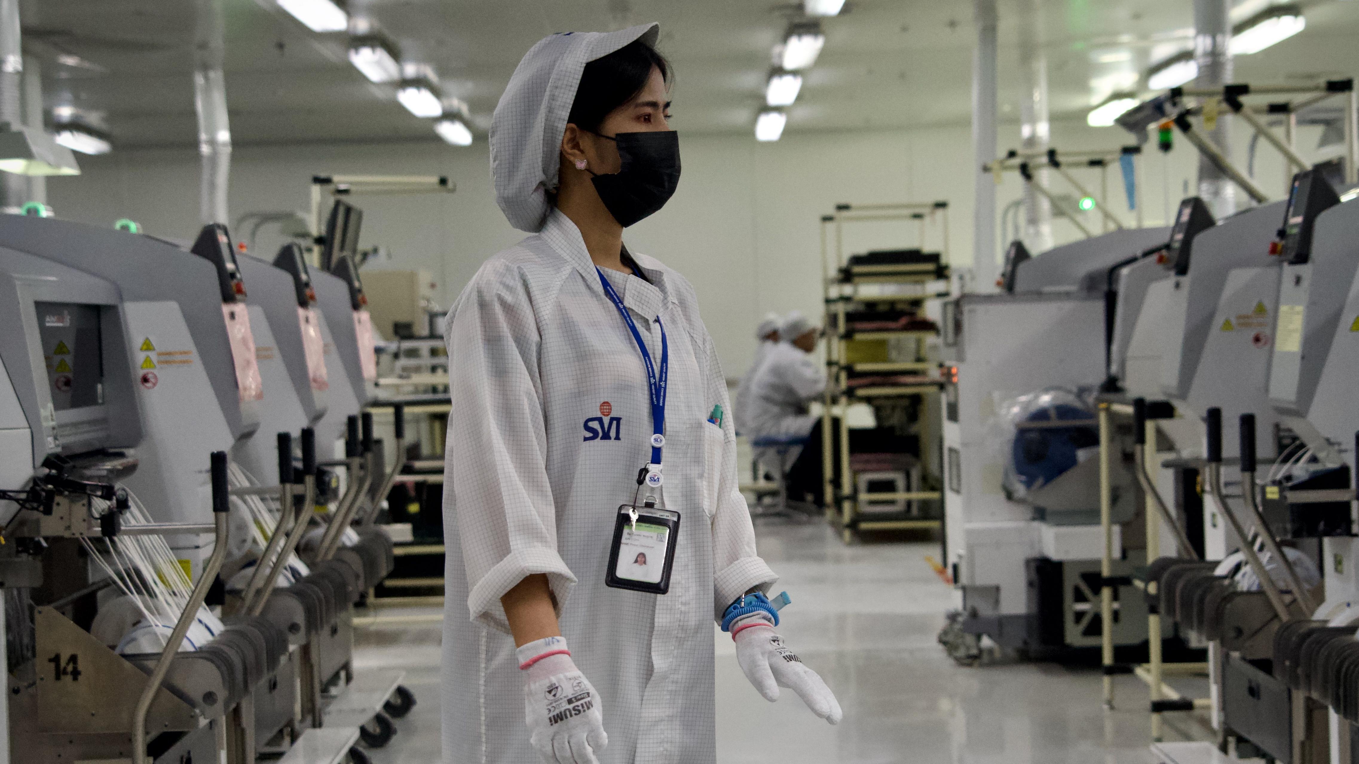 一名身穿工作服的工人站在電子工廠的機器排間