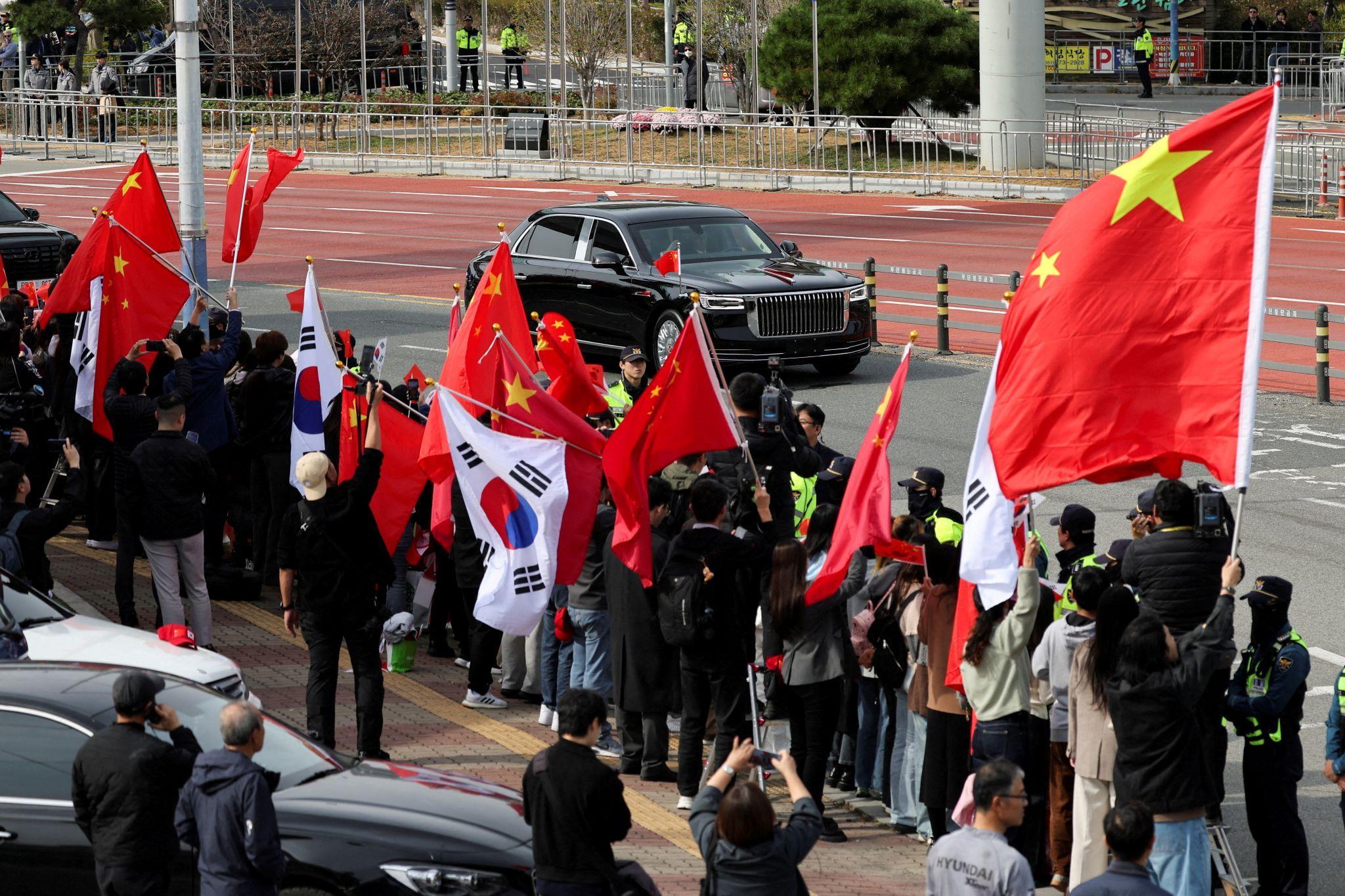 2025年10月30日，在韓國舉行的亞太經合組織（APEC）峰會期間，中國國家主席習近平與美國總統特朗普就貿易緊張局勢和雙邊關係舉行雙邊會晤後，車隊離開金海國際機場。人們揮舞著中國和韓國國旗。