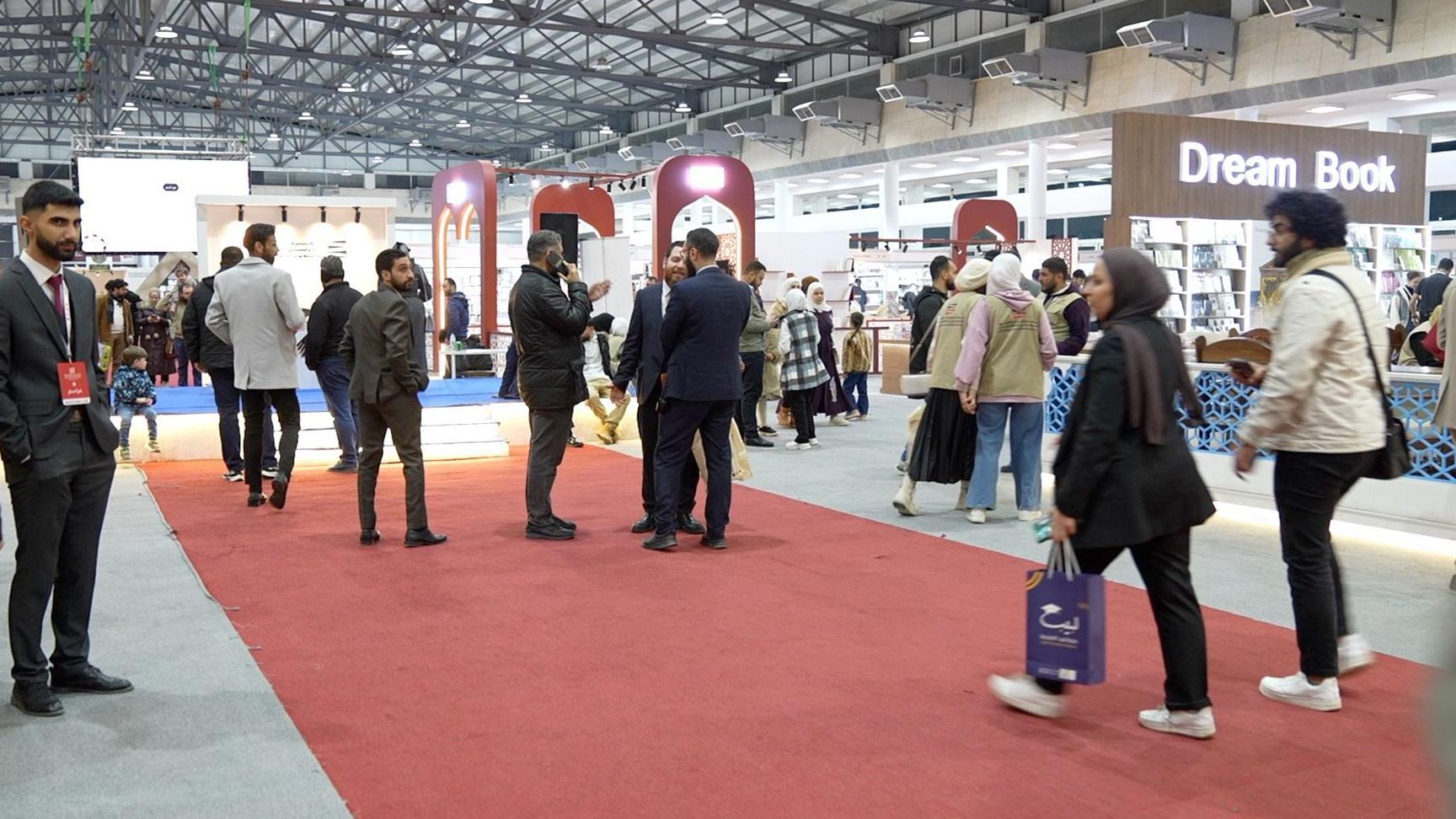 رجال ونساء يمشون ويتحدثون داخل معرض دمشق الدولي للكتاب 