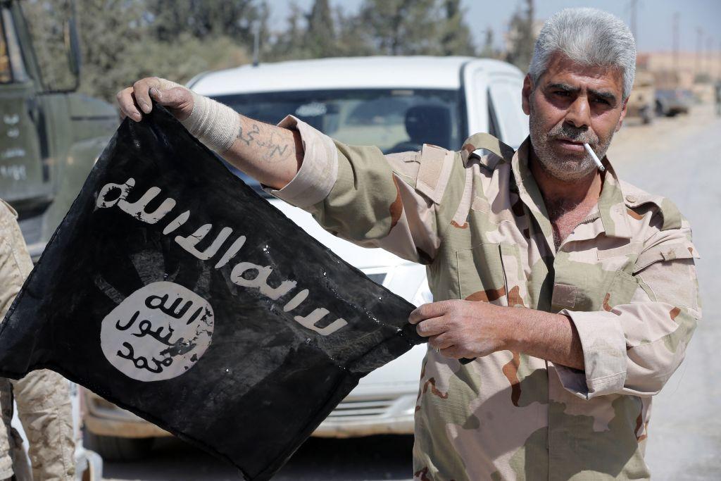 جندي سوري يرفع علم تنظيم الدولة الإسلامية في 4 أبريل/نيسان 2016، بعد أن استعادت القوات السورية السيطرة في اليوم السابق على بلدة القريتين، الواقعة في محافظة حمص وسط سوريا.