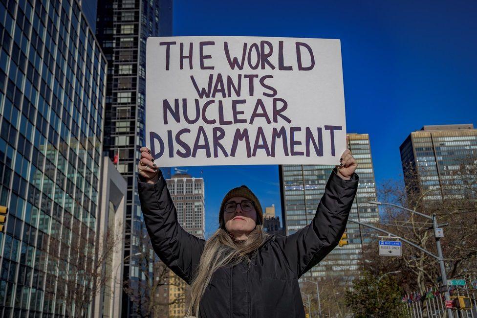 Una manifestante con una chaqueta negra muestra una pancarta que dice: "The world wants nuclear disarmament" 