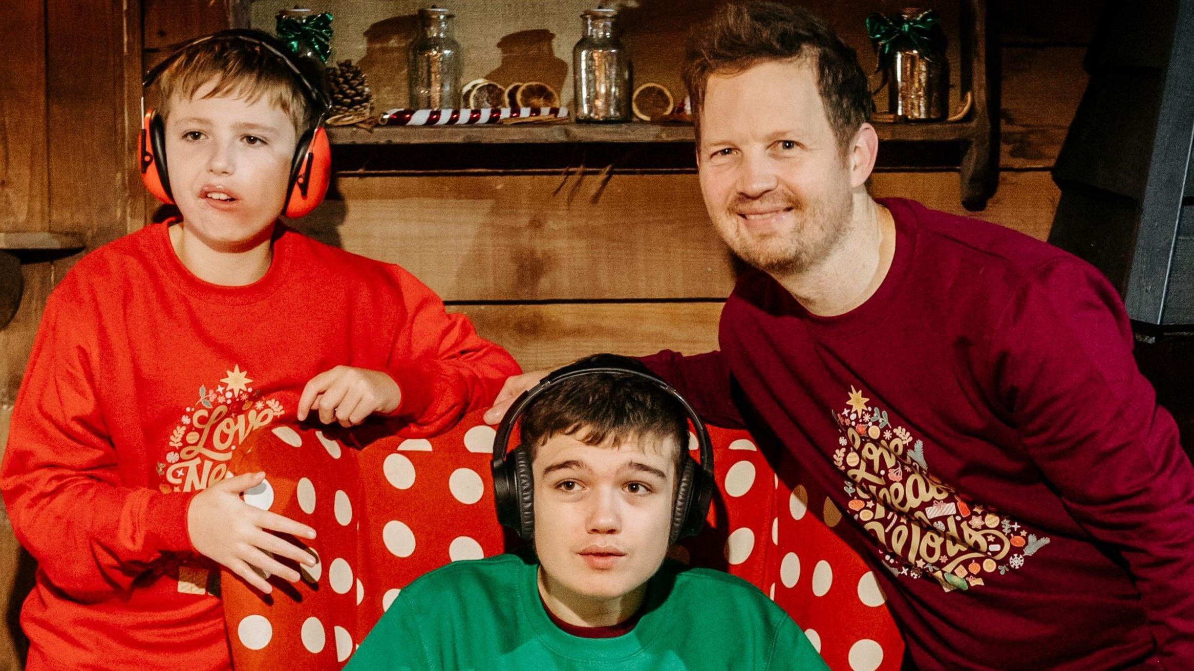 James com seus filhos. Eles vestem roupas com estampas de Natal nas cores verde e vermelha.