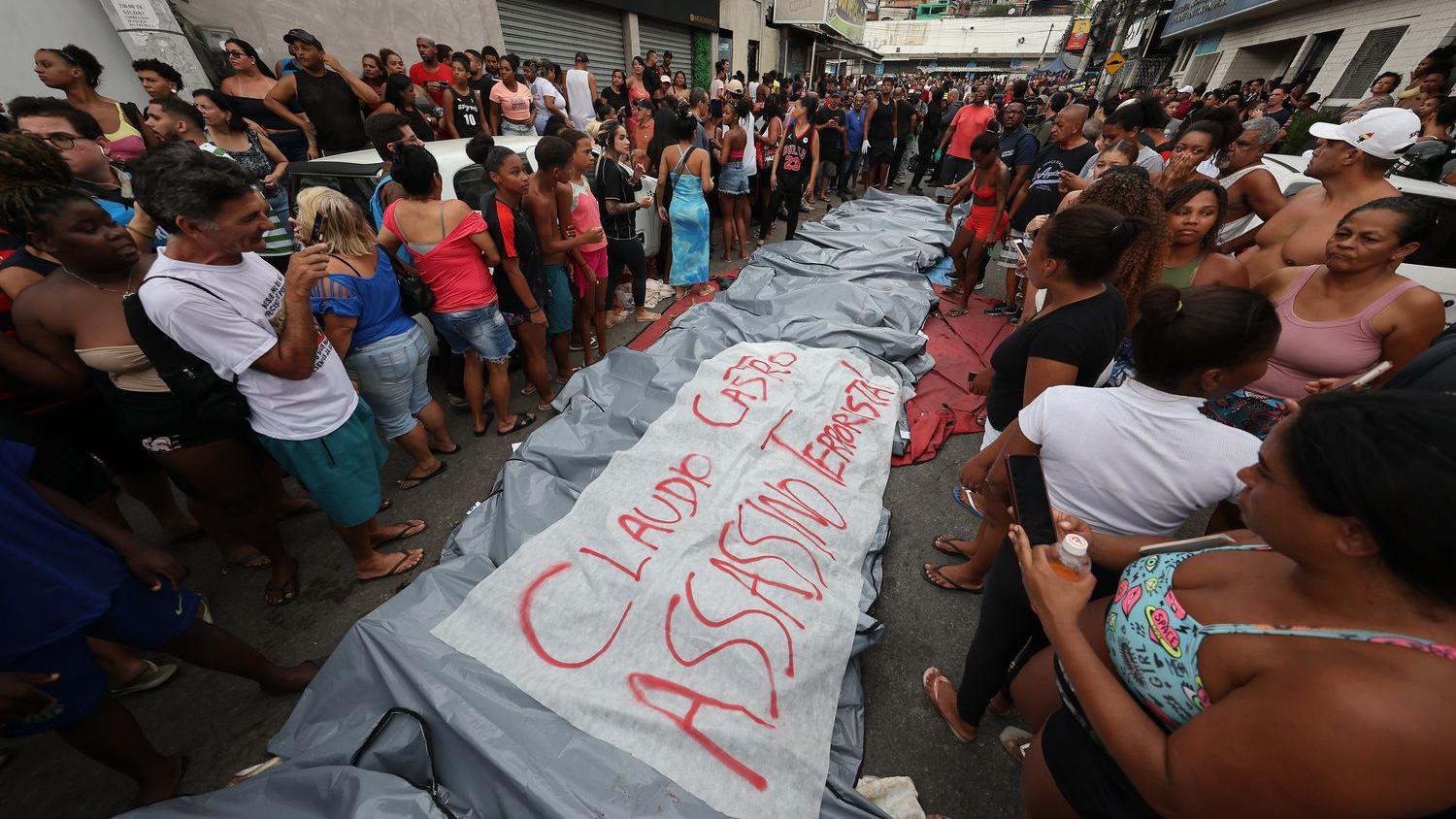 Personas se encuentran junto a los cuerpos de sus familiares asesinados por la policía junto a una pancarta que dice "Claudio Castro, asesino y terrorista", el 29 de octubre de 2025. 
