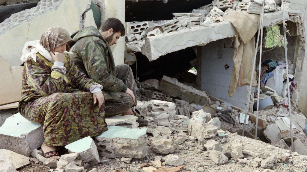 Seorang anggota Hizbullah dari komunitas Syiah Libanon duduk bersama ibunya di samping rumah mereka yang hancur di Sidikine, Libanon Selatan, 28 April 1996.