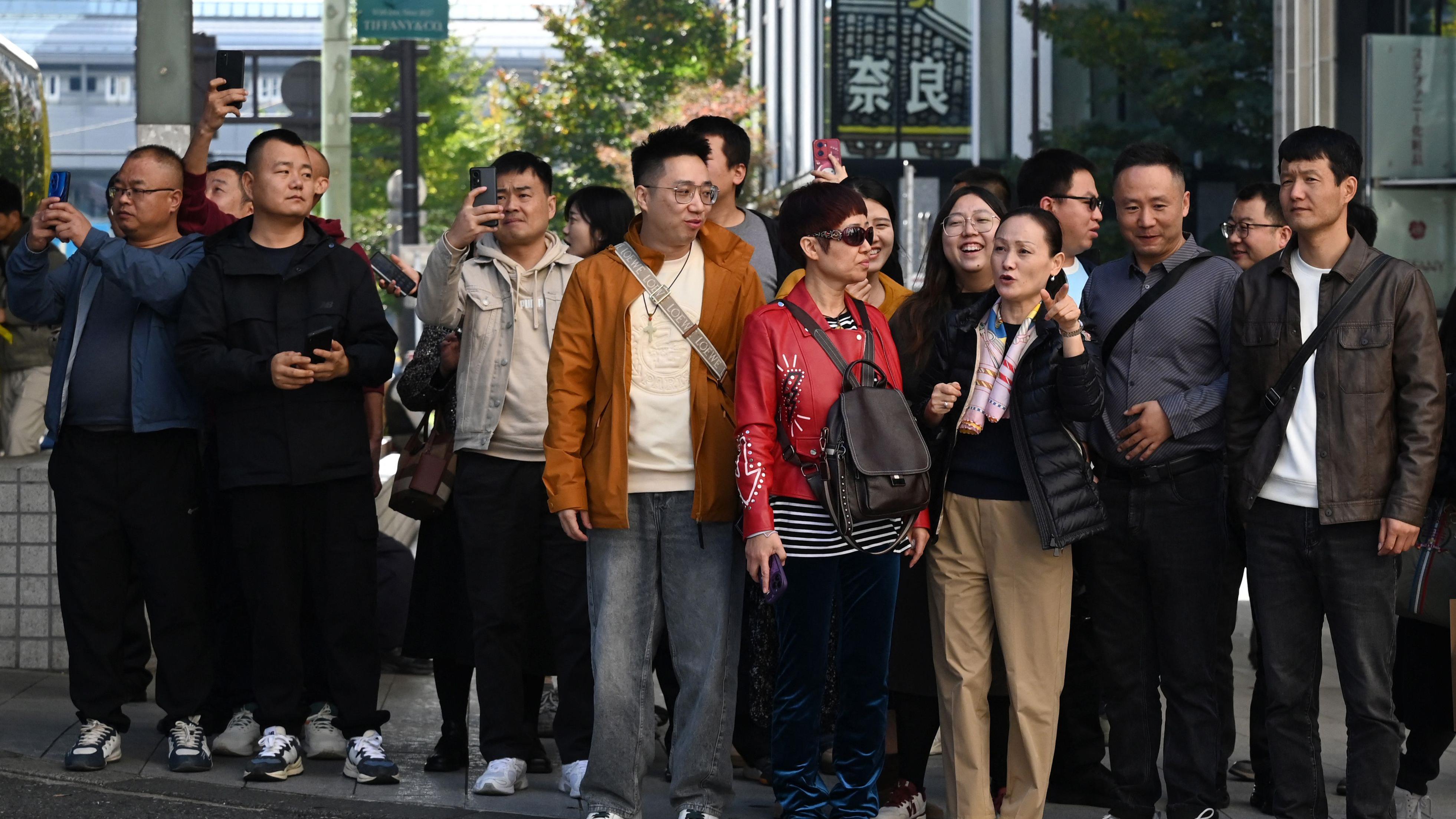 東京銀座購物區一群中國遊客舉起手機拍照，部分人在聆聽導遊講解（16/11/2025）