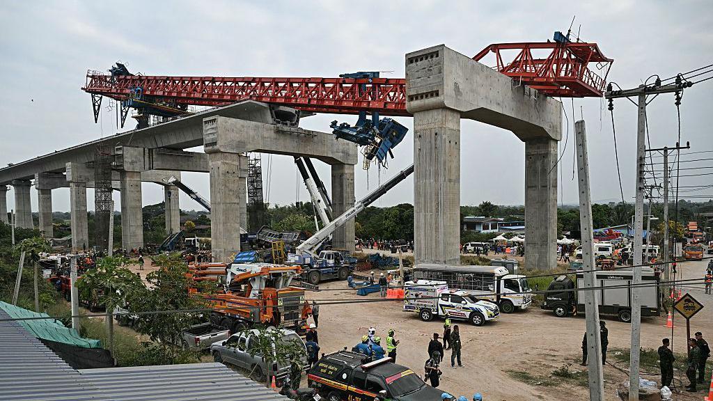 Para pekerja penyelamat berdiri di samping reruntuhan kereta api yang mengalami kecelakaan akibat tertimpa derek konstruksi di Provinsi Nakhon Ratchasima, Thailand, Rabu (14/01).