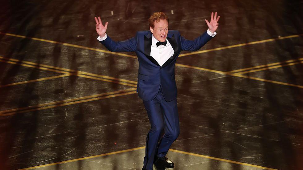 Konan O' Brajan na sceni u teget odelu, beloj košulji i crnom leptir mašnom