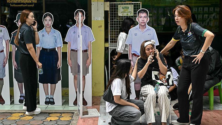 Dos mujeres asisten a otra en las afueras de un colegio en Thailandia.