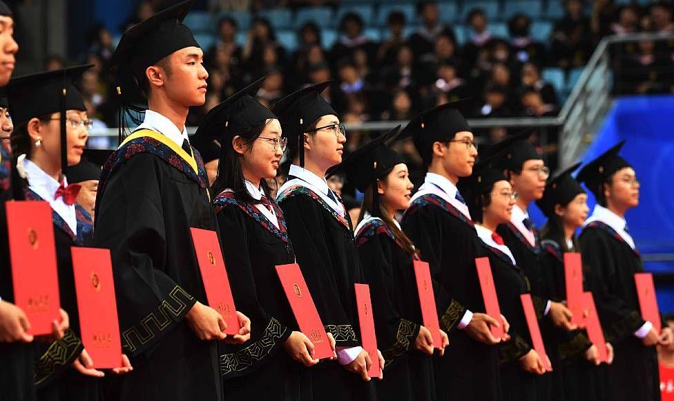 Jóvenes con togas muestran sus diplomas durante su ceremonia de graduación en la Universidad de Pekín 