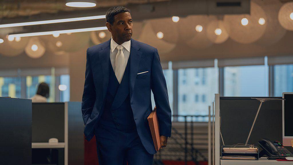 Cena do filme 'Luta de Classes', com Denzel Washington de terno e gravata, segurando pastas de trabalho