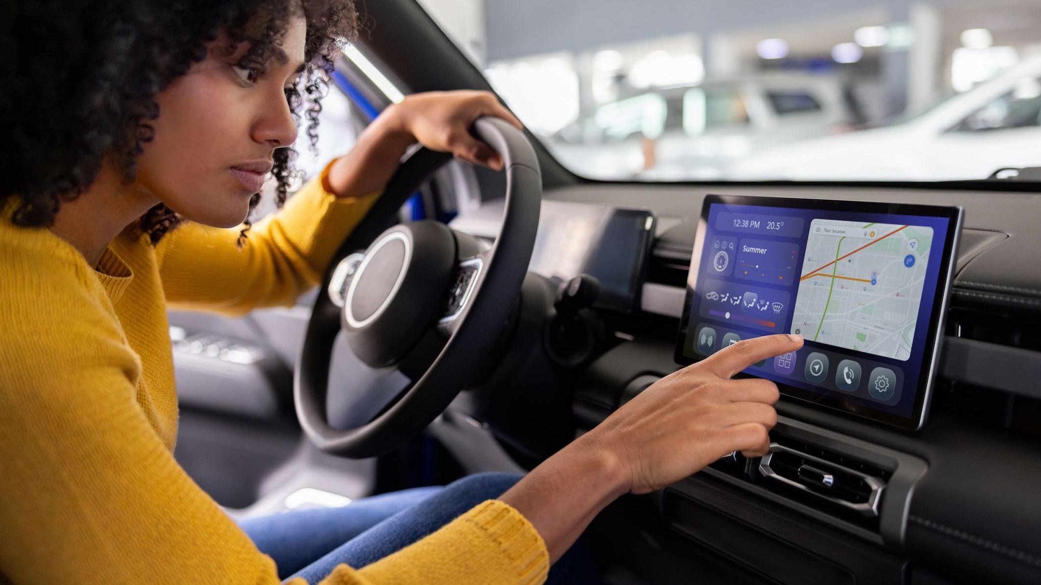 Una mujer señalando una pantalla en el interior de su coche. 