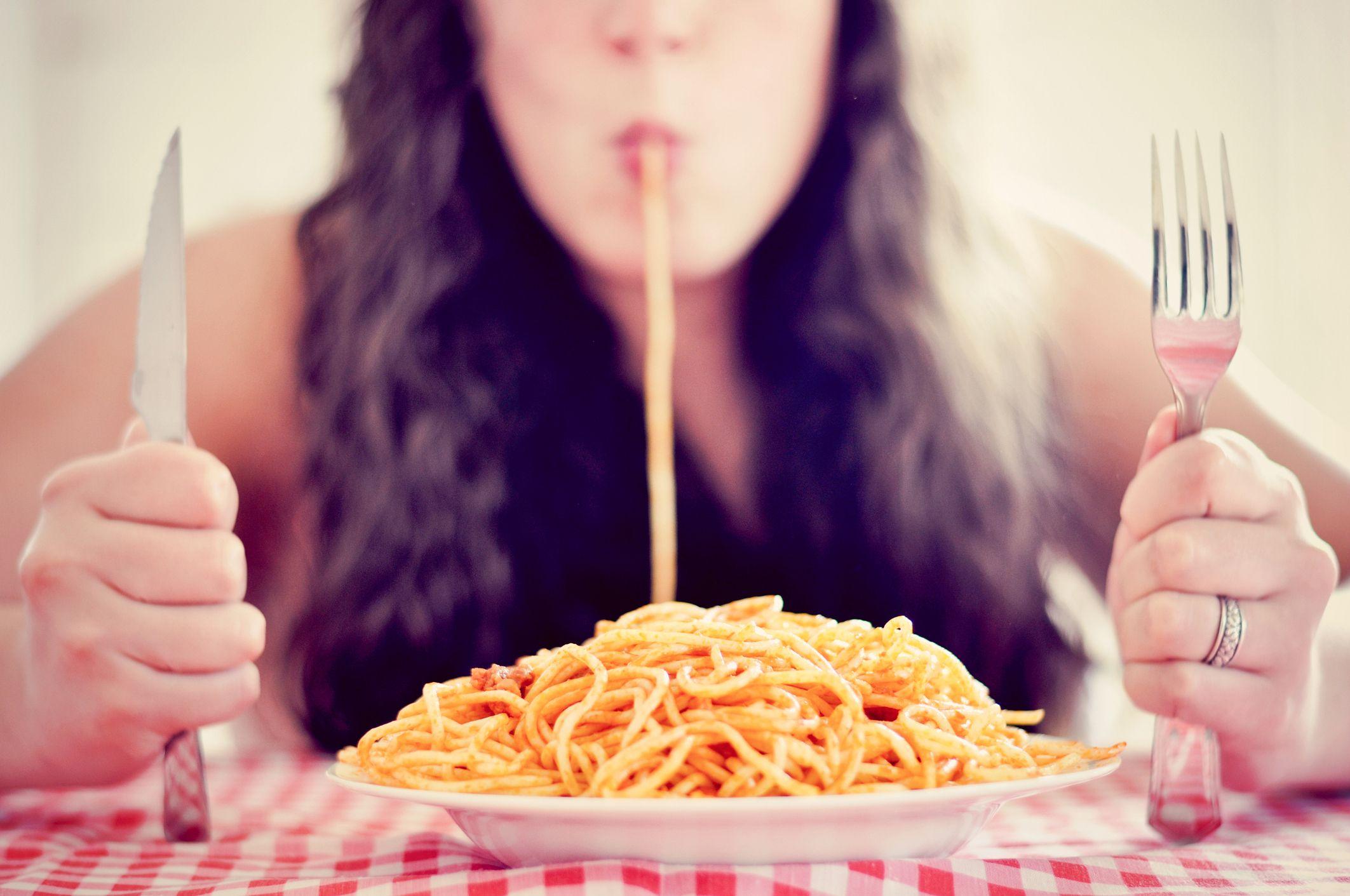 Mujer sorbiendo un espaguetti con frente a un plato de pasta. 