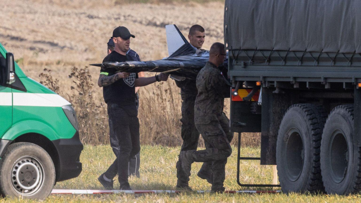  Três homens carregam um drone para dentro de um caminhão. 