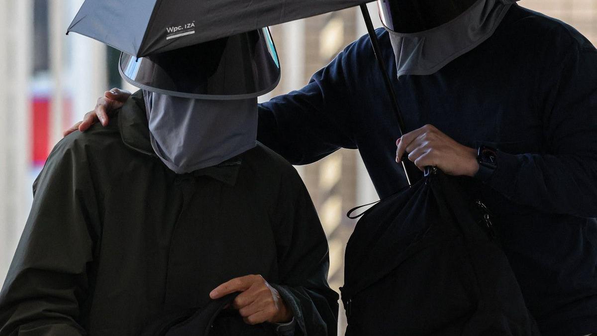 兩名身穿黑色外套、戴黑色帽子及口罩的男子共撐一把雨傘。