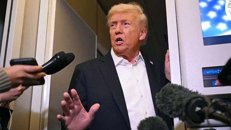 Donald Trump, de pie en el Air Force One, les habla a los reporteros. Varios micrófonos le rodean.