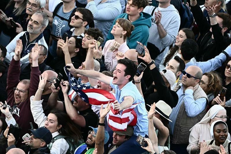 Multidão saúda o papa Leão 14 após o anúncio de sua eleição, com um homem segurando a bandeira dos Estados Unidos