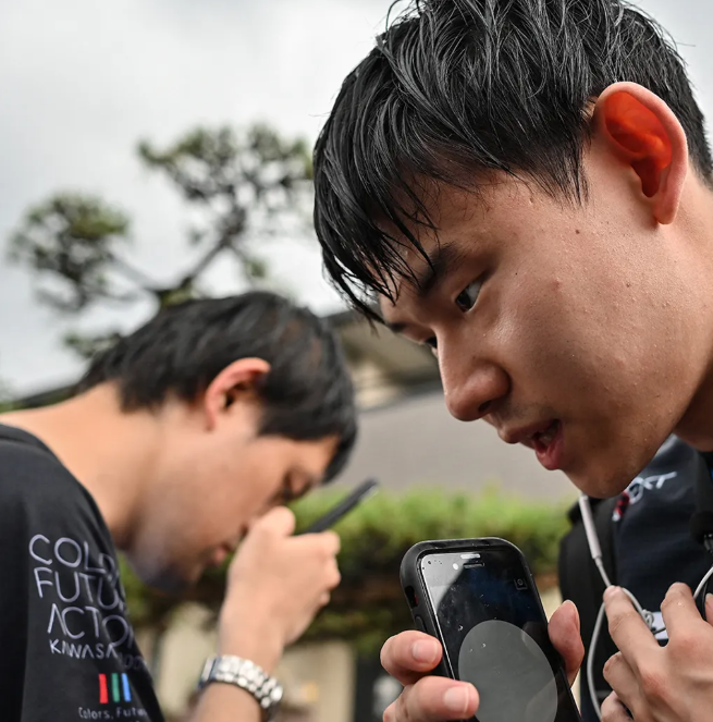 Dos personas con rasgos orientales y sus teléfonos muy cerca de su cara. 