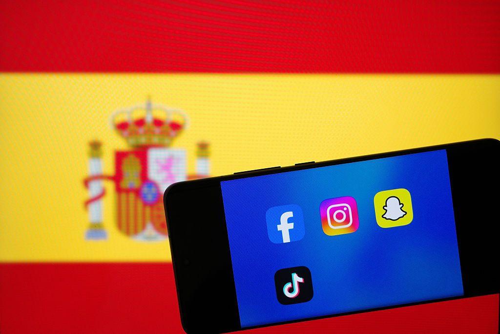Un teléfono con los iconos de algunas redes sociales sobre una bandera de España en segundo plano. 