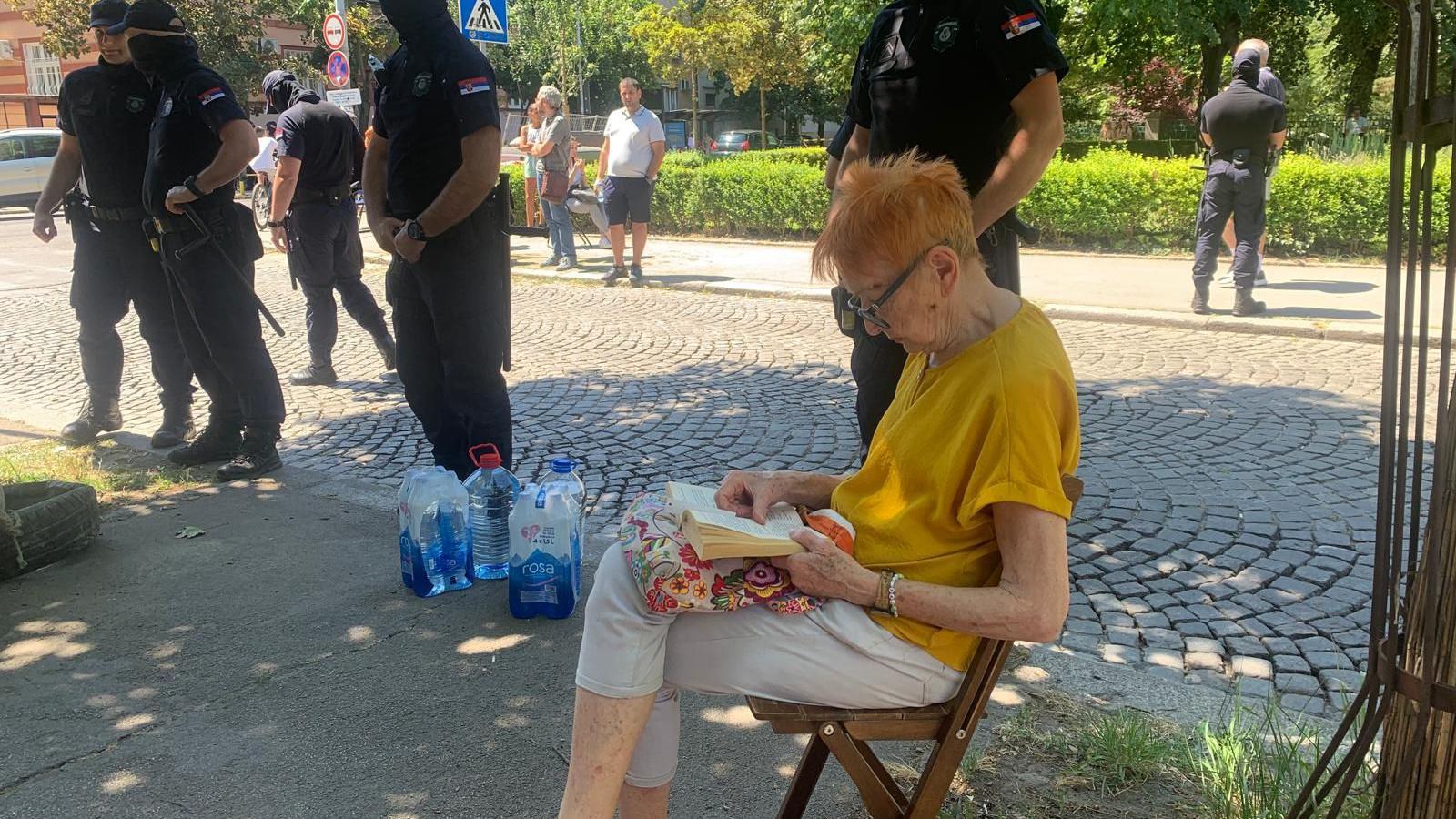 Baka sedi na trotoaru i čita knjigu, pored nje policija