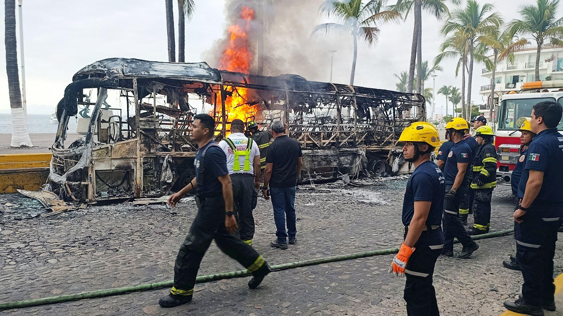 Um &ocirc;nibus em chamas no M&eacute;xico, cercado por bombeiros e um caminh&atilde;o do corpo de bombeiros