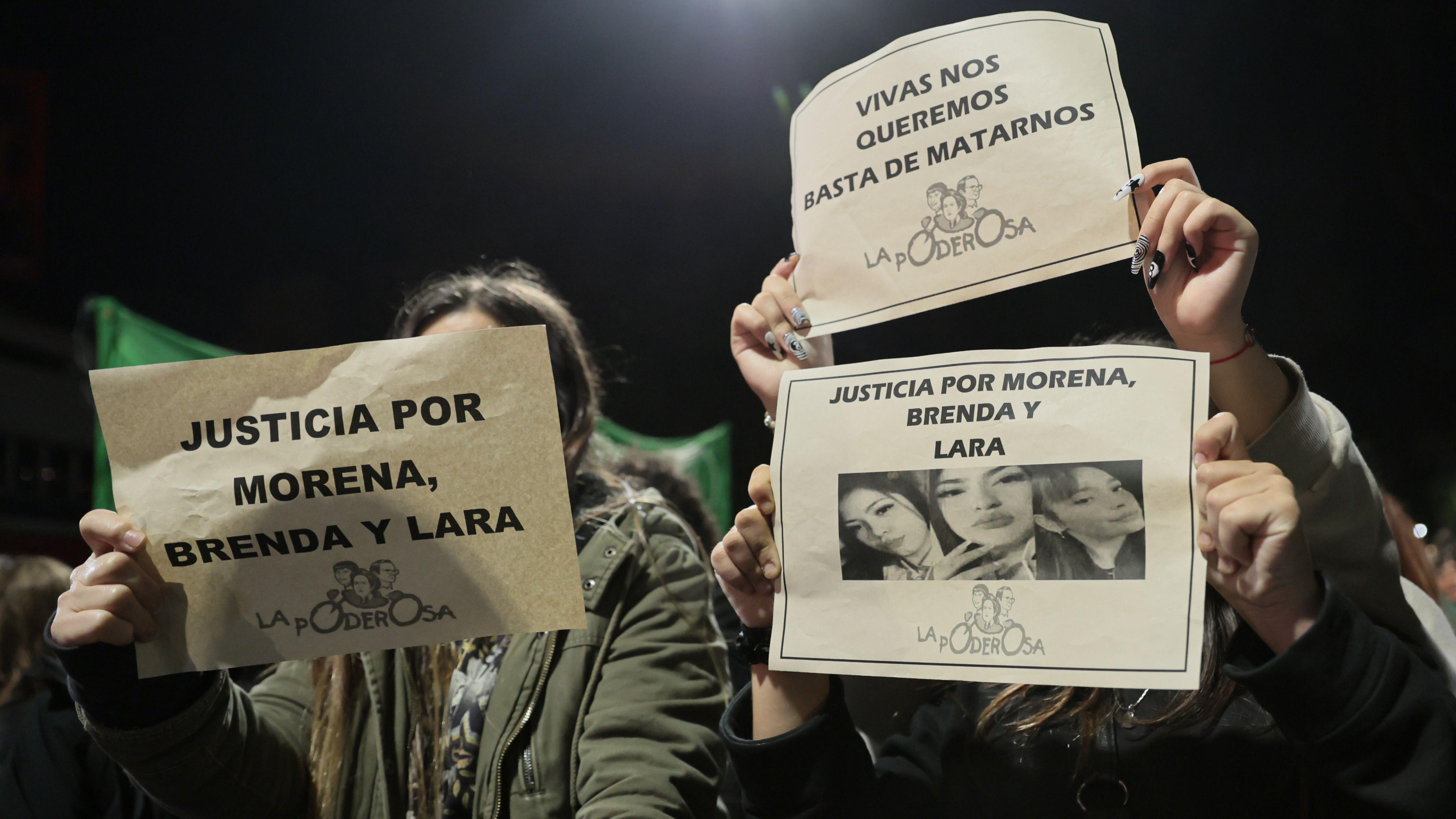 Tres manifestantes sostienen carteles durante una protesta por el asesinato de las tres mujeres argentinas. En los carteles se lee "Justicia por Morena, Brenda y Lara" y "Vivas nos queremos, basta de matarnos".