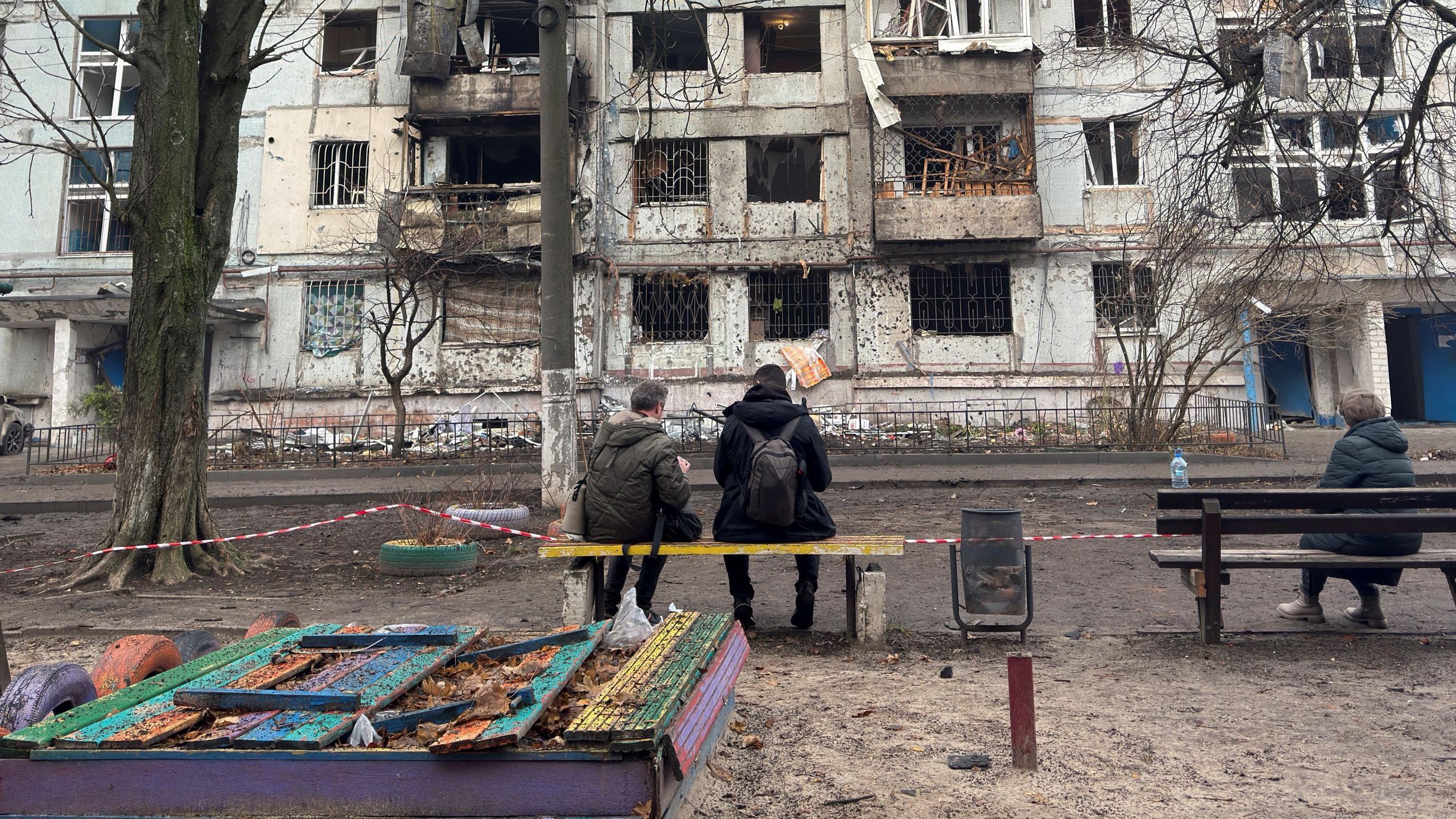 ljudi sede na klupi ispred zgrade posle ruskih napada 