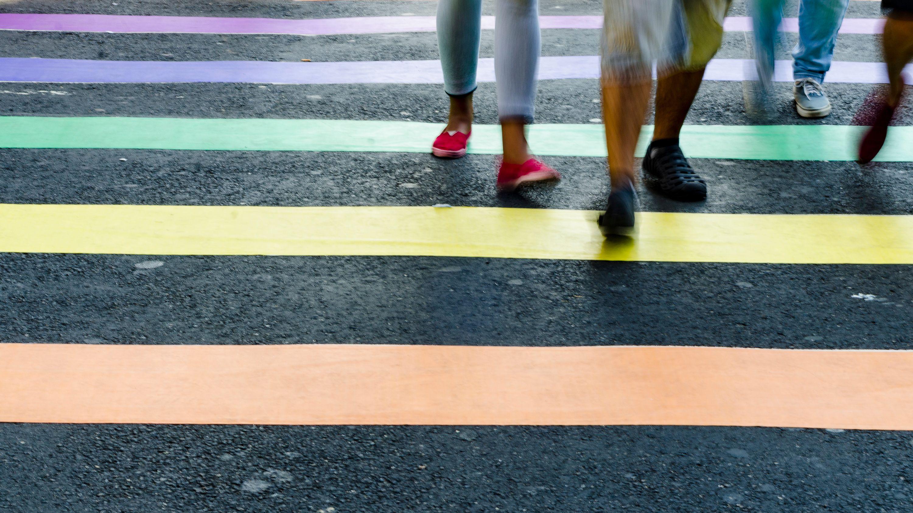 Pessoas caminham sobre faixa de pedestre pintada com as cores da bandeira LGBT