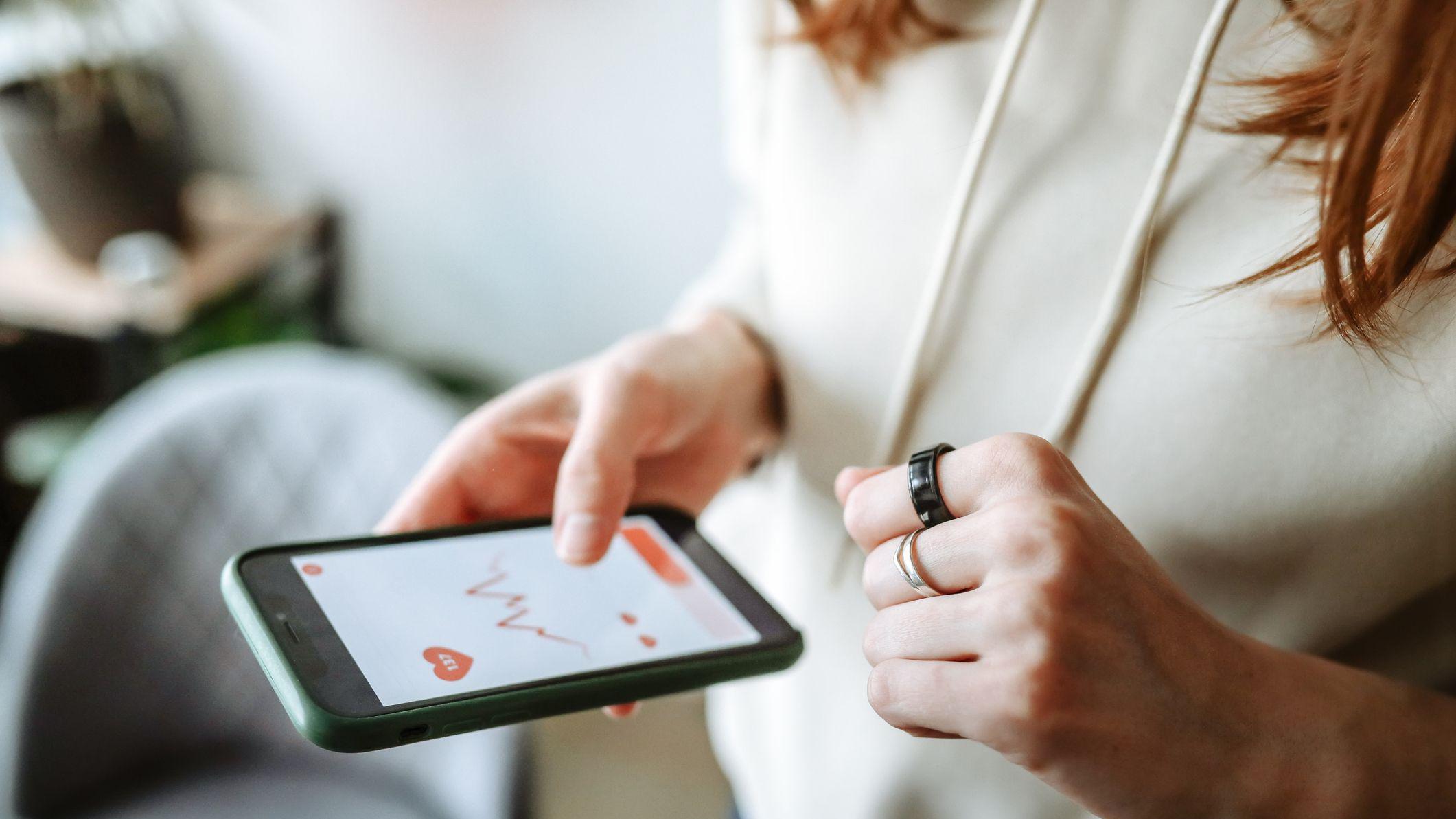 Mulher usando um anel inteligente e verificando seus dados de sa&uacute;de no aplicativo de celular